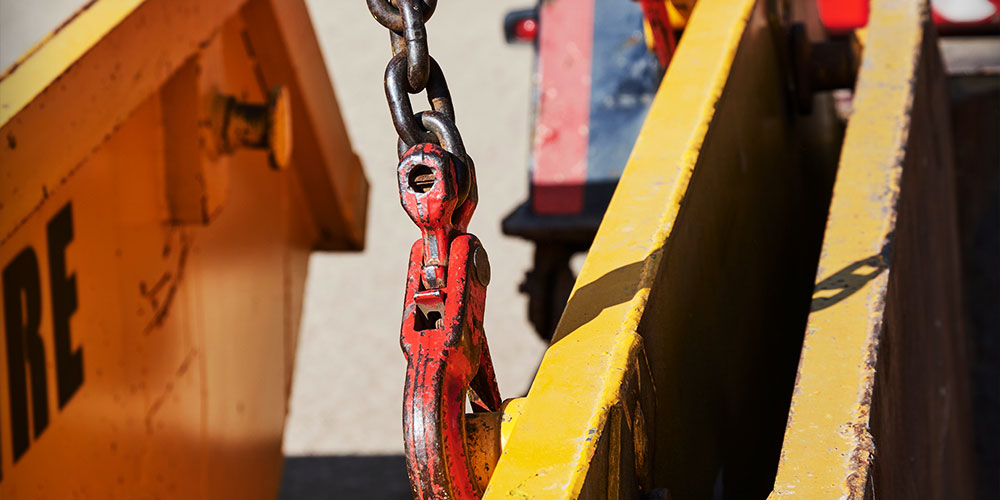 A yellow and red skip featuring a chain, positioned on a dirt road